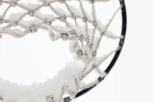 Looking up through the net from below. An unused basketball net with fresh snow on the netting. Selective focus. Gray sky background.