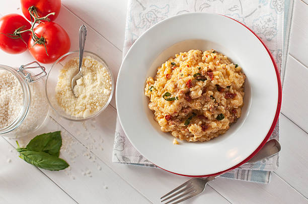 Bowl of tomato and sausage risotto with ingredients on table stock photo
