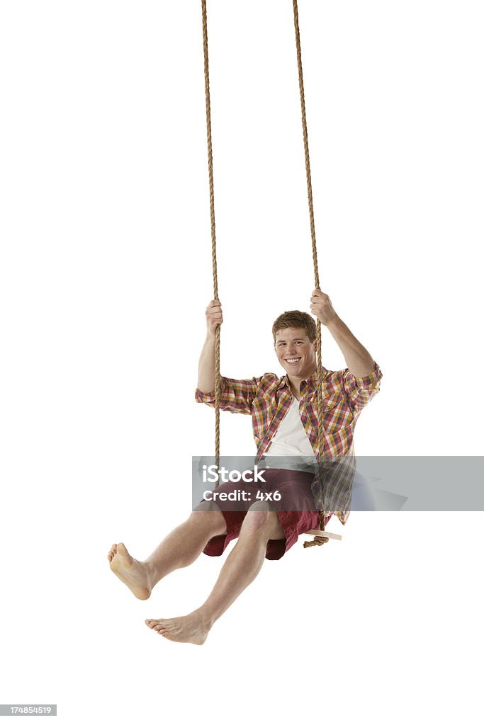 Beau jeune homme souriant se balancer sur une corde - Photo de Corde pour se balancer libre de droits