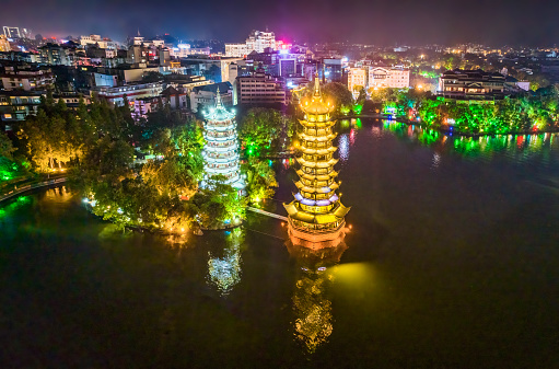 Aerial view  of Beautiful bright illuminated Sun and Moon Twin Pagodas at the Shan Lake - Shanhu - in Guilin. Guilin's Sun and Moon Twin Pagodas are one of the Guilin's main attractions. The word sun and moon in Chinese character written together meant brightness. People say it symbolizes that the future of Guilin is bright. The Sun Pagoda is constructed out of copper, has 9 floors and reaches a height of around 41 metres. The Moon Pagoda's construction is mainly made of marble; has 7 floors and measurer around 35 meters high. The twin pagodas are connected via a tunnel at the bottom of the lake. Colorful Illuminated Guilin Landmark and Tourist Attraction at Night. Guilin, Guangxi, China.