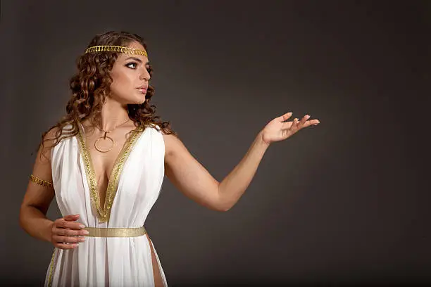 "The Beautiful Young Woman Wearing White and Gold Greek Costume, Looking to Something on her Left  on the Dark Background ."