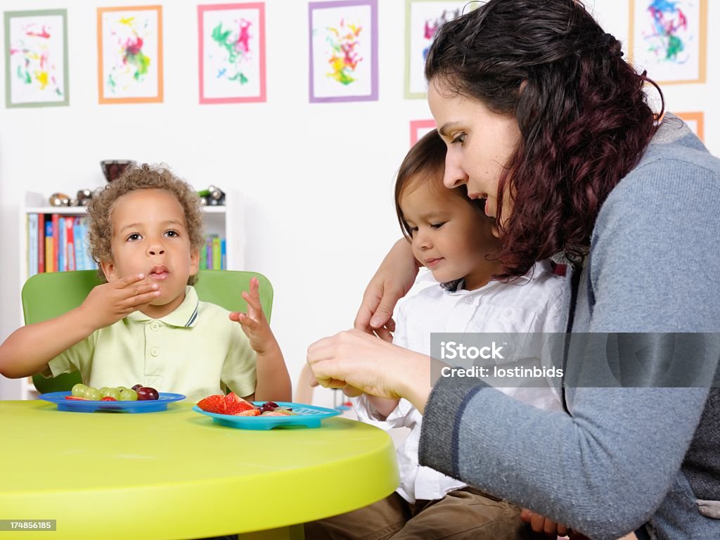 Caucasian Carer Assisting Toddler At Mealtime A protrait a caucasian carer assisting toddler at mealtime. Child Stock Photo