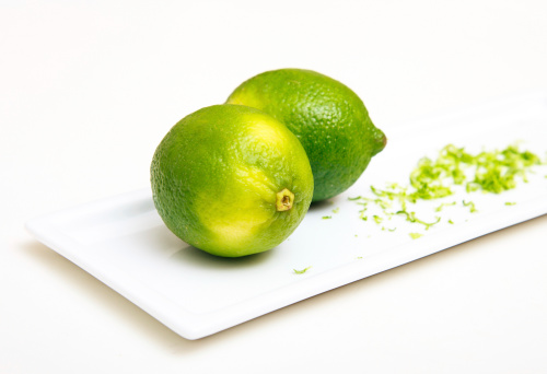 Limes with green lemon shavings in white plate on white background.