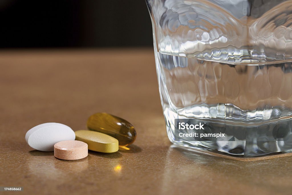 Vitamin Tablets "Vitamin pills or tablets and a glass of water on a table - including fish oil, multivitamin, calcium and vitamin C - shallow depth of field." Calcium Stock Photo