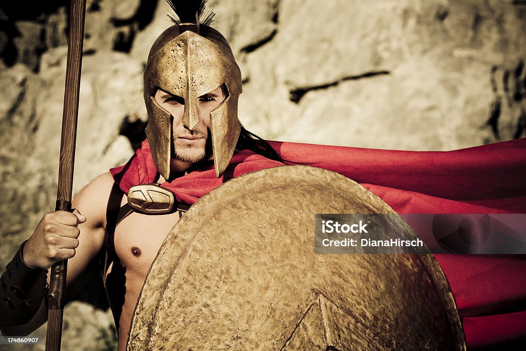 Portrait of Spartan warrior with shield and lance "Portrait of Spartan warrior with selfmade theater clothings and with original spartan symbol, adopted in the 420s BC, was the letter lambda (a), standing for Laconia or Lacedaemon, which was painted on the Spartans' shields and broochs,selective focus, very creative sepia - color retouching to underline the ancient time,vignetting and added noise" Sparta - Greece Stock Photo