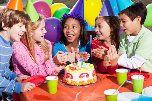 Multi-ethnic children (7-10 years) having fun at birthday party.  Lit candle (number 8) on the cake.