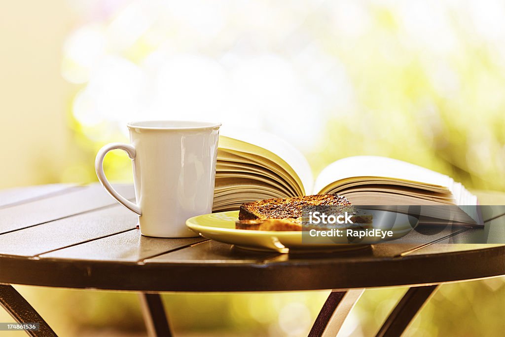 Perfect relaxation with book, buttered toast and steaming drink "A hardback book, a tea or coffee mug, and a plate of buttered toast sit on a garden table in the sunshine -  perfect for a relaxing break!" Accessibility Stock Photo