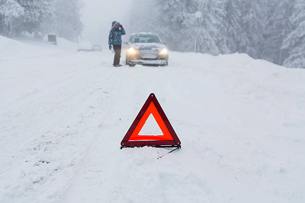 istock Woman loking at her broken car in snow blizzard...warning triangle 174861673