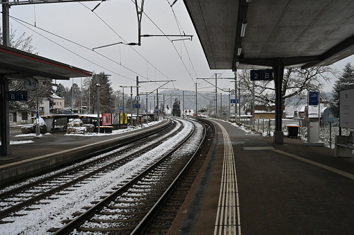 Urdorf, Switzerland- 12 18 2022: Railway platform and rails of a small village station in winter. There is snow on the railway tracks.