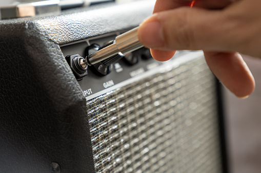 Close up of electric guitar amplifier with hand is plugging a cable into jack. Shallow depth of field