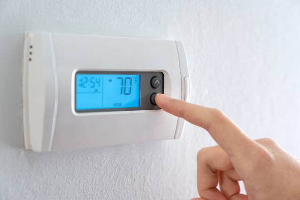 Hand press indoor room thermostat to lower the temp stock photo