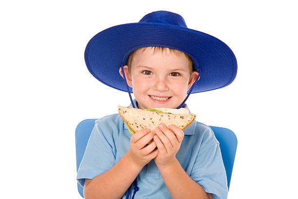 School Boy Lunch Time A little Australian school boy having a healthy lunch. Isolated on white. food elementary student healthy eating schoolboy stock pictures, royalty-free photos & images