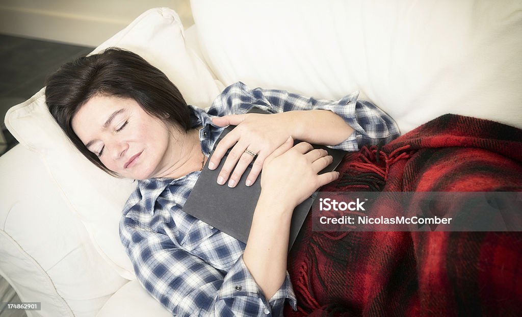 Housewife in her 40s sleeping on couch with book Housewife in her 40s sleeping on the couch with a book in her arms. 40-49 Years Stock Photo