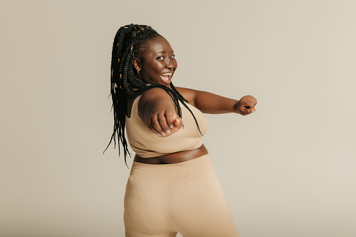 Rear view of voluptuous African woman in sportswear exercising on studio background