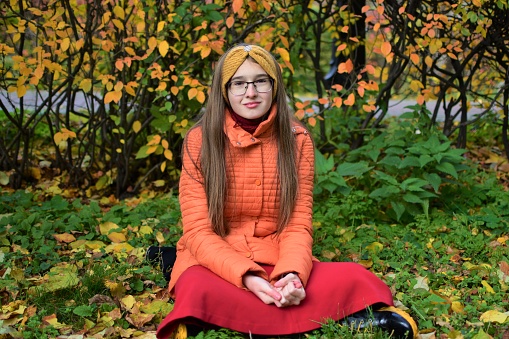 A beautiful girl is sitting on the grass with an autumn park.