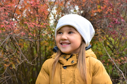 Portrait of a beautiful little girl in warm clothes. The child looks away and laughs. Autumn landscape with bokeh in the background.
