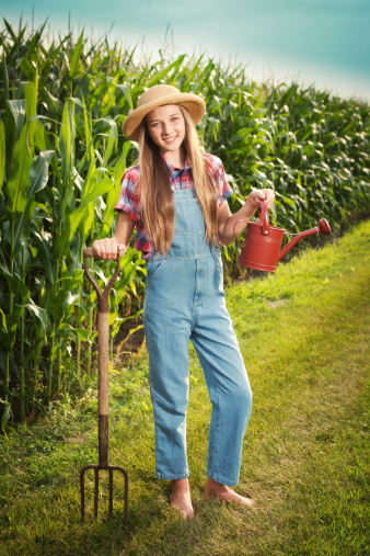 Subject: A farm girl holding a garden watering can in front of a corn field.