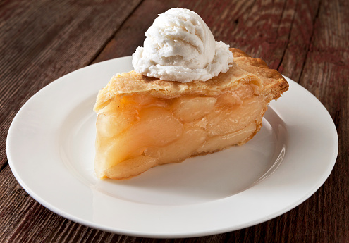 A slice of apple pie with vanilla ice cream on a rustic table top.