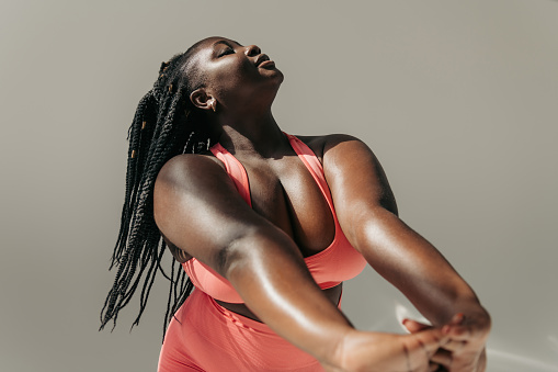 Attractive African plus size woman in sportswear doing stretching exercises in fitness studio