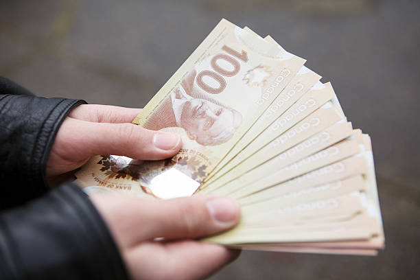 Hands holding Canadian hundred dollar bills outside. Closeup of a persons hands holding and fanning out several hundred dollar bills. canadian currency photos stock pictures, royalty-free photos & images