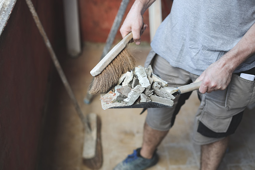 Young caucasian unrecognizable man holding a small broom of construction debris on an old shovel, close-up side view. The concept of cleaning and installing windows, construction work, home renovation.