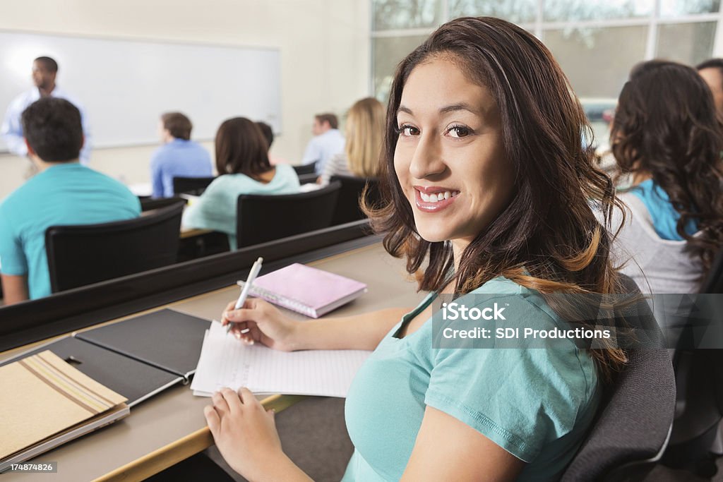 College age girl taking notes during professor's lecture in class Adult Stock Photo