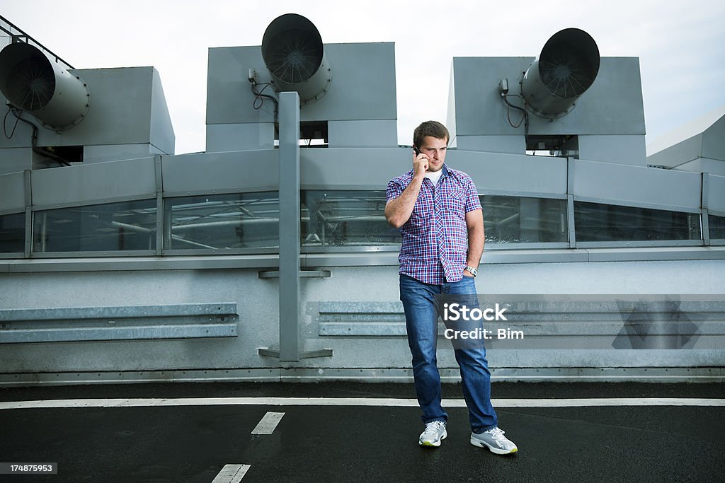 Jovem Homem Casual usando telefone celular no estacionamento na cobertura - Foto de stock de Canal de Ar royalty-free