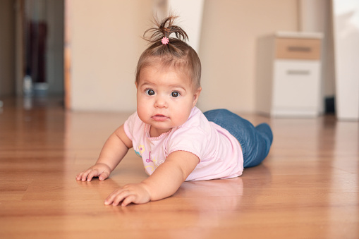A seven-month-old girl is trying to crawl. The cute, little baby is at home, and she is playing on the floor.