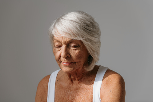 Portrait of confident gray hair senior woman in tank top looking away against background