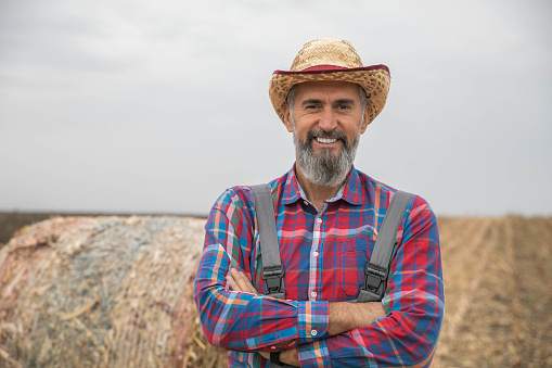 Portrait of confident middle-aged farmer. Business success in the corn field. In the background bales of corn.