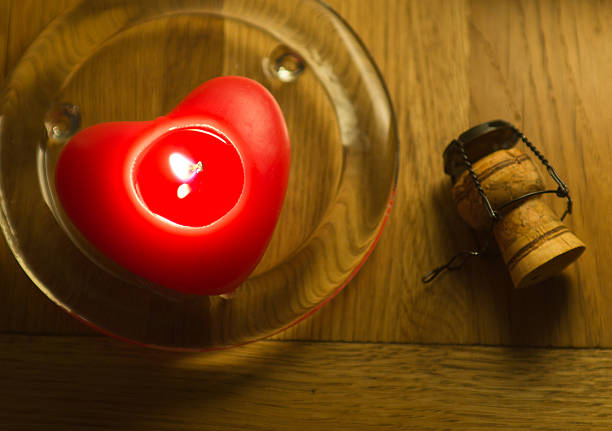 Red heart shaped candle on a glass stand with champagne cork.