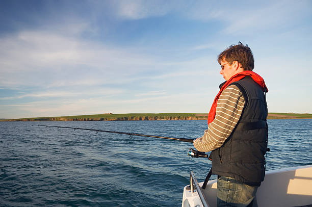 Angling from a boat "Young man fishing from a boat in Scapa Flow, Orkney Islands, Scotland. Lots of copy space." sea fishing stock pictures, royalty-free photos & images