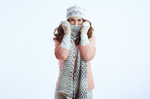 Hello winter. stylish female in sweater, mittens, hat and scarf wrapping up in a scarf isolated on white.