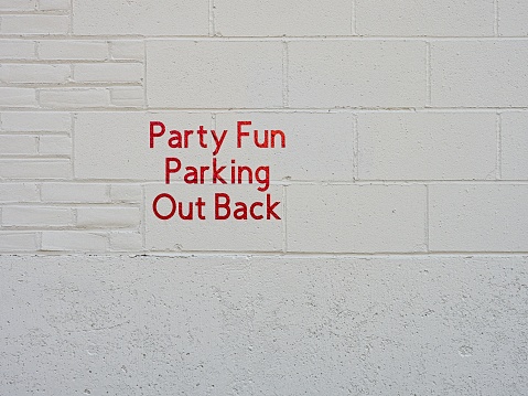 Humorous sign on side of white concrete wall depicting where to have fun. Business sign suggestive of party fun to be found out back, a design and concept image with copy space.