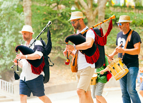 Pipers and drummer wearing straw hats, playing as they walk in a folk street band in a traditional festival, public park in  Santiago de Compostela, A Coruña province, Galicia, Spain.