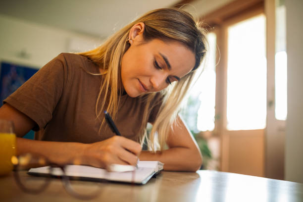 istock Young woman writing in notebook at home 1748872424