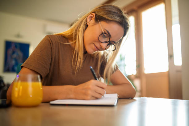 istock Young woman writing in notebook at home 1748872430