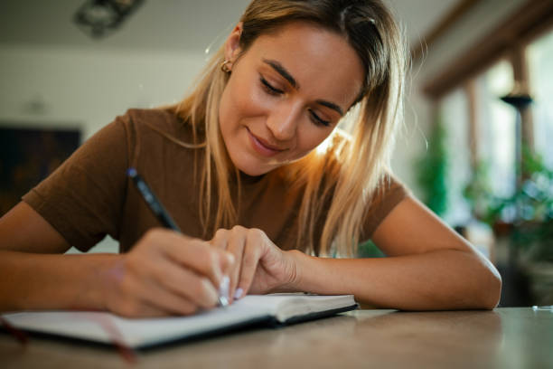 istock Young woman writing in notebook at home 1748890197