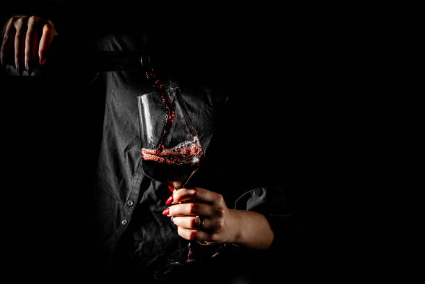 mains de femme versant du vin rouge dans un verre à partir d’une bouteille sur fond noir - Photo