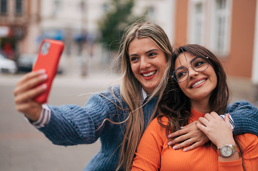 Two beautiful girls taking selfie while walking down the street