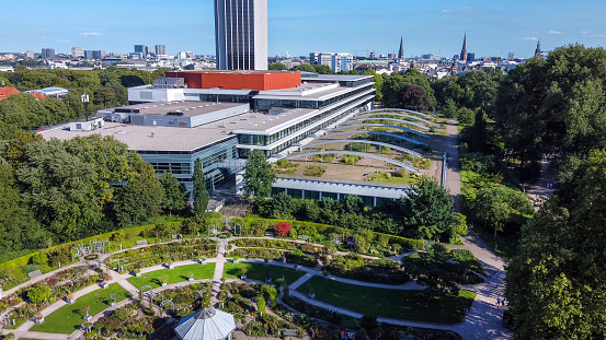 Awe  drone point of view  on Circles of the rose garden of the Botanical Garden Planten un Blumen  and garden on the roof of some building (maybe hotel). People in distance (relaxing on green grass)