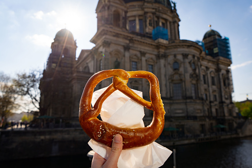 Close-up of large bavarian pretzel being held up at sunset with Berliner Dom in the background