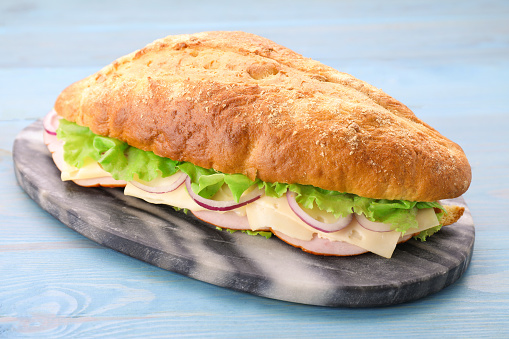 Delicious sandwich with fresh vegetables and cheese on light blue wooden table, closeup