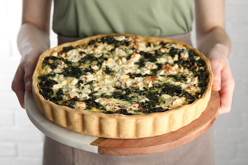 Woman holding delicious homemade spinach quiche on light background, closeup