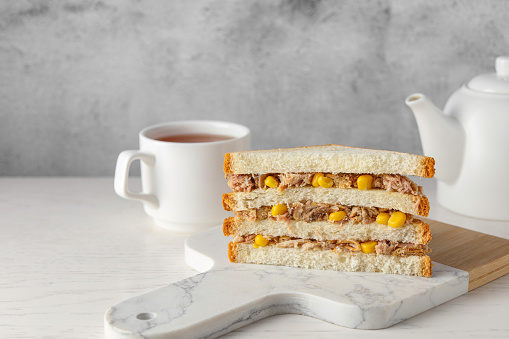 Delicious sandwich with tuna and corn on white wooden table, space for text