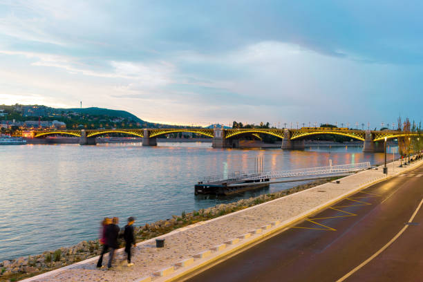 el puente margit y el río danubio al anochecer con gente caminando por la orilla del río en budapest, hungría - margit bridge fotos fotografías e imágenes de stock
