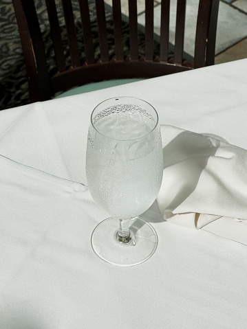 Glass of water sweats in summer heat at fine restaurant on linen table cloth