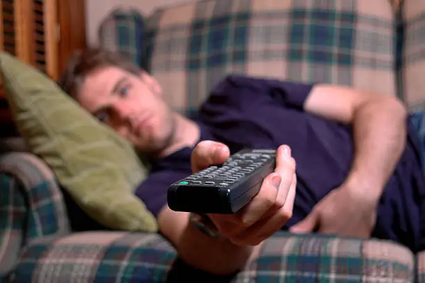 "A young man flips channels while lying on a couch. Shallow depth of field, focus on the remote control.Also available:"