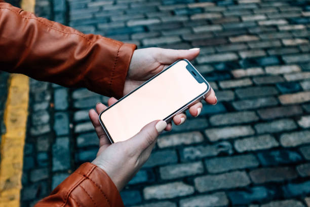 istock Woman's hand Holding small modern smartphone on Cobblestone Street UI Mock Up - Two Hands Side On 1748961560