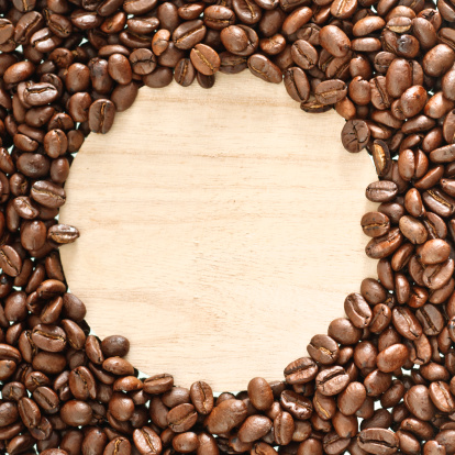 Roasted coffee beans in front of a wooden background with copyspace.